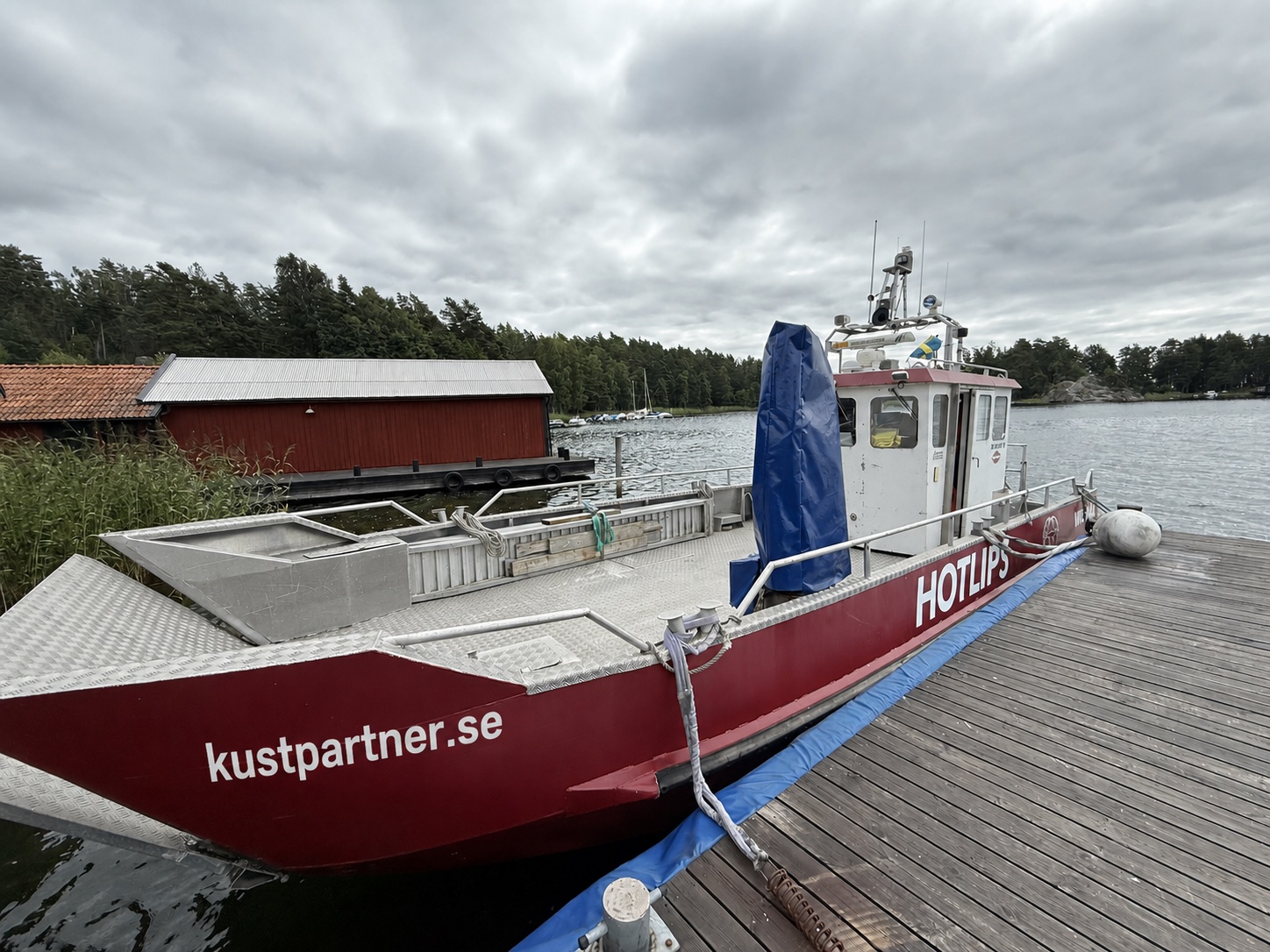 Arbetsbåten Hot Lips med Kustpartner-märkning vid brygga i skärgårdsmiljö